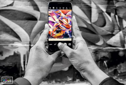 Manos en blanco y negro fotografeando graffiti de color con el móvil